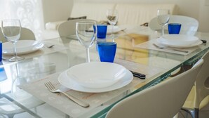 Une table à manger dressée avec de l’argenterie blanche, des verres bleus et des couverts, avec une cloison en verre au premier plan.