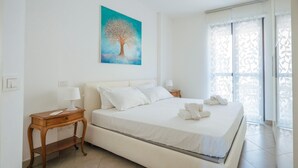 Une chambre à coucher comprenant un lit, deux tables de chevet, une commode, un tableau et une fenêtre donnant sur un paysage.