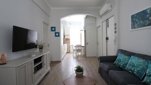 Una sala de estar con un televisor de pantalla plana, un sofá con cojines estampados, una mesa de centro y una planta en maceta.