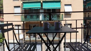 Un balcón con una mesa y dos sillas, con vistas a un edificio con balcones y toldos.