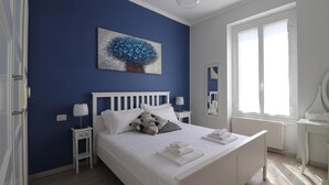 Un dormitorio con una cama blanca, una pared azul y un cuadro de un árbol.