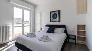 Una habitació d'hotel amb un llit gran, vista a la ciutat a través d'una porta corredissa, un quadre a la paret i una petita taula de nit.