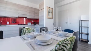 Una cuina moderna amb rajoles vermelles, zona de menjador amb taula blanca preparada per a quatre persones i una cadira blava.