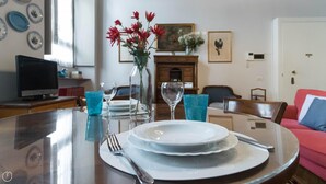 Una mesa de comedor dispuesta con platos, cubiertos y vasos, con un florero de flores sobre la mesa.
