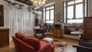 Una sala de estar acogedora con un sofá rojo, una mesa de comedor y un televisor. Hay platos decorativos en la pared y una araña.