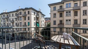 Un balcón con una mesa y sillas de madera, con vista a una calle con coches estacionados y edificios.