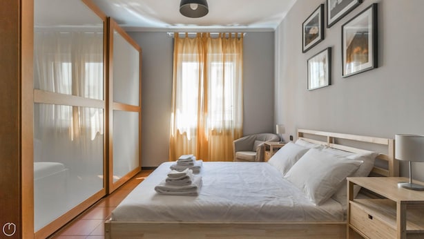 Una habitación de hotel con una cama grande, una mesita de noche con lámpara, una silla y un armario.