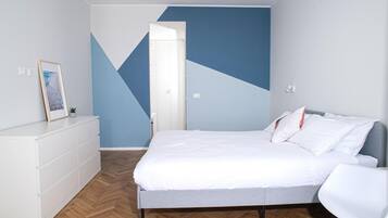 Un dormitorio moderno con una cama, un aparador blanco, una silla y un diseño geométrico en la pared.