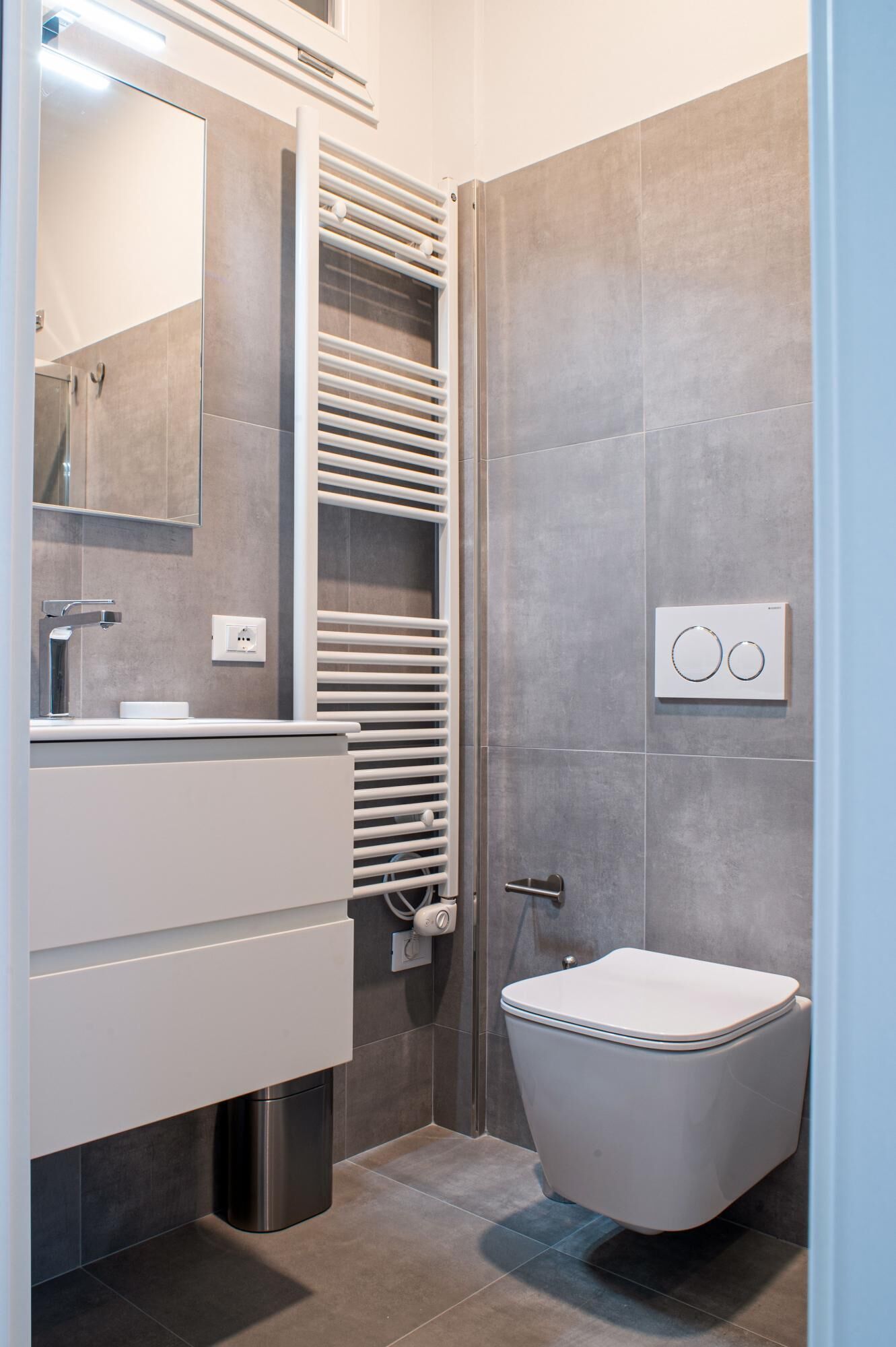 Un baño moderno con inodoro, lavabo, espejo, toallero y zona de ducha.