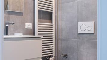 Un baño moderno con inodoro, lavabo, espejo, toallero y zona de ducha.