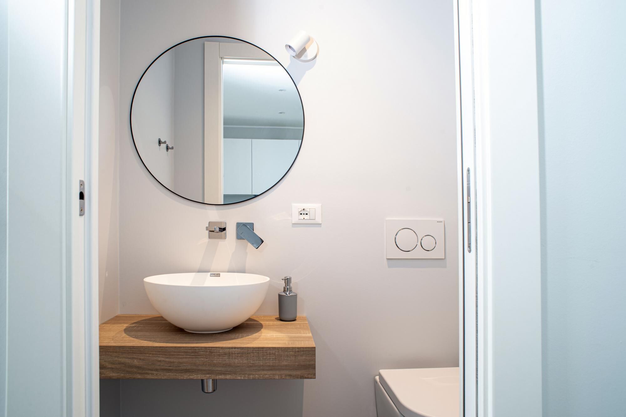 A bathroom with a round mirror, a white sink, and a toilet.