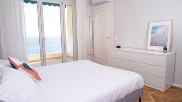 Une chambre avec un lit, une commode et une vue sur la mer, visible à travers une porte-fenêtre coulissante.
