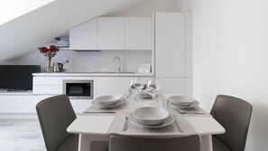 Une cuisine moderne avec des meubles blancs, un four à micro-ondes encastré et un évier. On y trouve une table à manger mise avec des assiettes, des verres et des couverts.