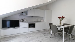 Une cuisine moderne avec des meubles blancs, un four encastré et un téléviseur à écran plat.