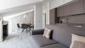 Una sala de estar moderna con un sofá gris, una mesa de comedor con sillas y una zona de cocina con armarios y un lavabo.