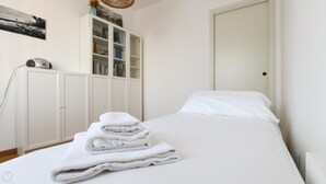 A neatly made bed with white linens and a stack of folded towels. - Colombo 4 (Villasanta)