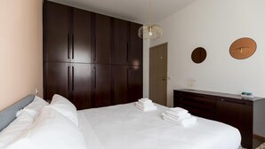 A hotel room with a large bed, dark wooden wardrobe, a small desk with a mirror, and a round wall decoration. - Quarnaro 2 (Monza)