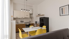 A compact kitchen with white cabinets, a black refrigerator, and a dining area with yellow chairs.