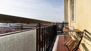 A balcony with a metal railing, a small table with a chair, and a view of the cityscape. - Quarnaro 2 (Monza)