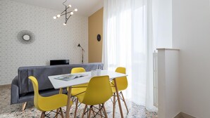 A modern dining area with a white table, yellow chairs, a grey sofa, and a geometric patterned wall. - Quarnaro 2 (Monza)
