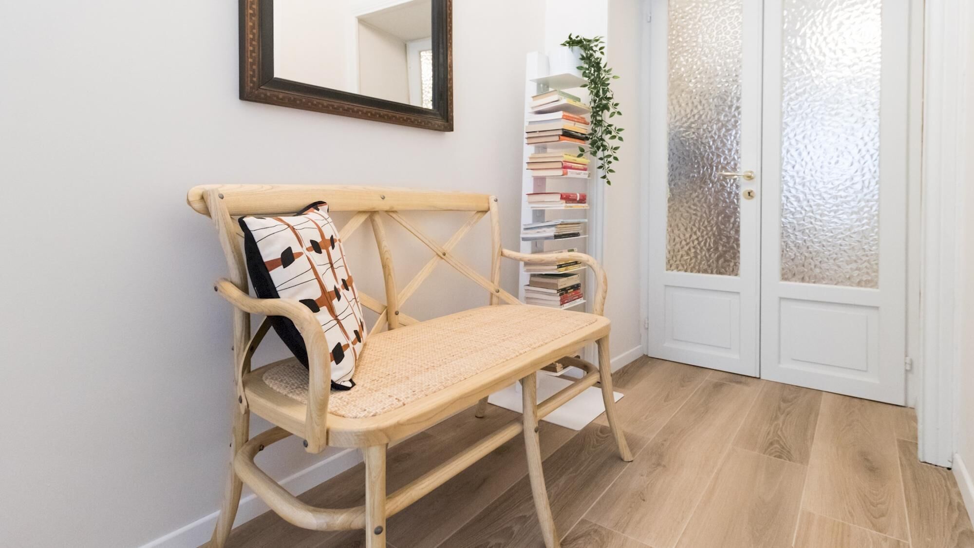 A wooden bench with a woven seat and backrest, positioned in front of a white door with frosted glass panels.