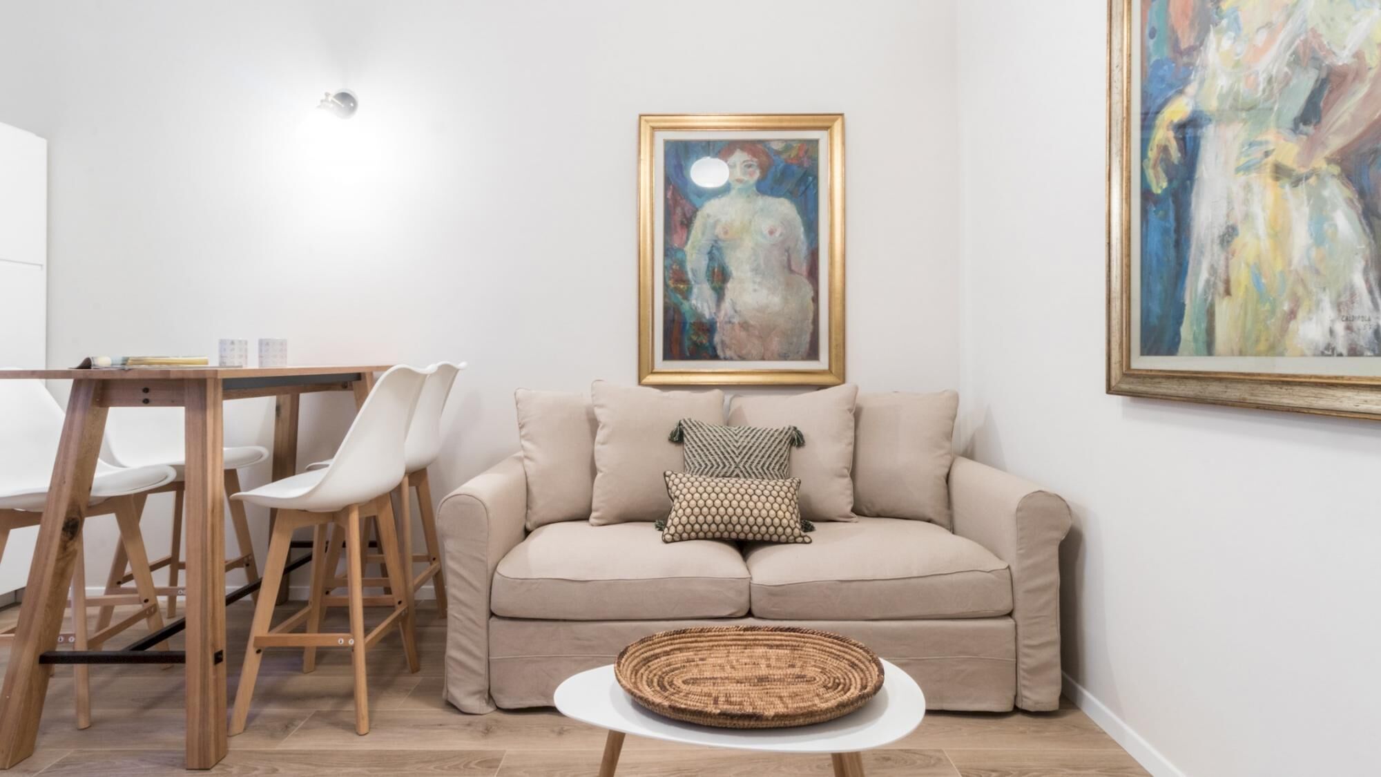 A living room with a beige sofa, a round woven coffee table, and a painting on the wall.