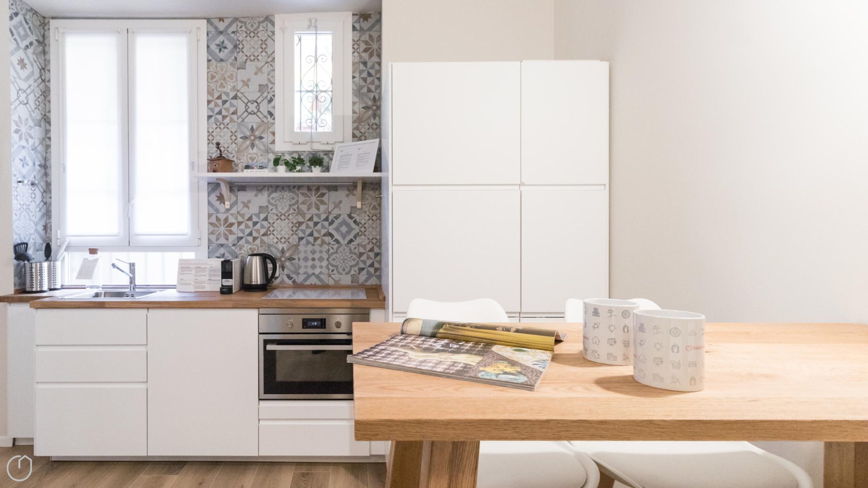 Una cocina moderna con armarios blancos, encimera de madera y una mesa de comedor con una revista y tazas de café.