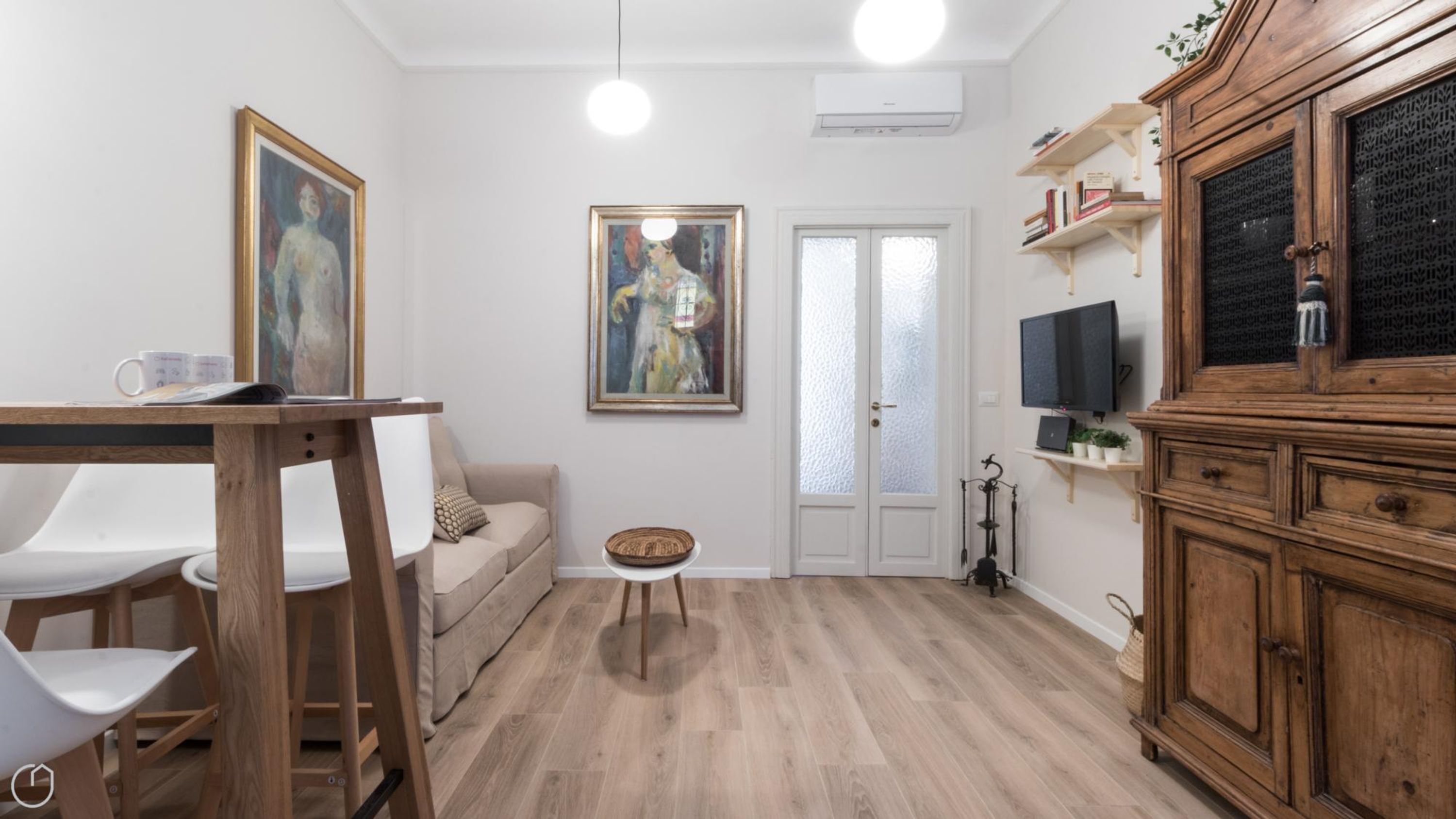 A modern living room with a wooden dining table, a sofa, a small round table, and a TV mounted on a wooden cabinet.