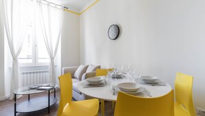 A dining area with a round table set for four, yellow chairs, and a clock on the wall. - Italianway Easy - Buenos Aires 65 B (Milan)