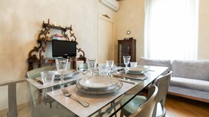 Taula de dinar preparada amb plats, gots i coberts, amb una televisió i objectes decoratius al fons.