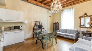 A compact living space with a kitchenette, a dining area with a glass table, a sofa, and a chandelier.