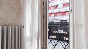 A view through a window with a radiator, a black metal fence, and a building with balconies in the background.