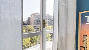Vista desde un balcón con barandilla metálica, una puerta blanca y un edificio con varios balcones al fondo.