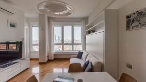 A modern living room with a large window, a sofa, a dining table, and a TV. - Italianway Easy - Biancamano 2 (Milan)
