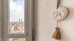 A window with a cityscape view, a white wall with a decorative plate, and a door handle. - Italianway Easy - Biancamano 2 (Milan)