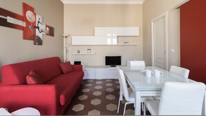 A modern living room with a red sofa, a glass dining table with white chairs, a flat-screen TV, and a kitchen area with white cabinets and a microwave. - Italianway Comfort - Borsieri 11 B (Milan)