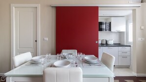 A dining area with a glass table set for four, white chairs, and a red partition. - Italianway Comfort - Borsieri 11 B (Milan)