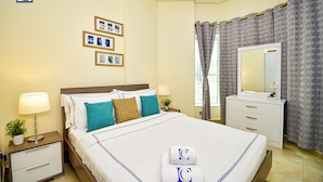 A hotel room with a neatly made bed, a bedside table with a lamp, a dresser with a mirror, and a wall with framed pictures. - ELN - Cozy Budget Studio in JLT Metro (Dubai)
