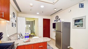 A modern kitchen with granite countertops, a stainless steel refrigerator, and wooden cabinets. - ELN - Cozy Budget Studio in JLT Metro (Dubai)