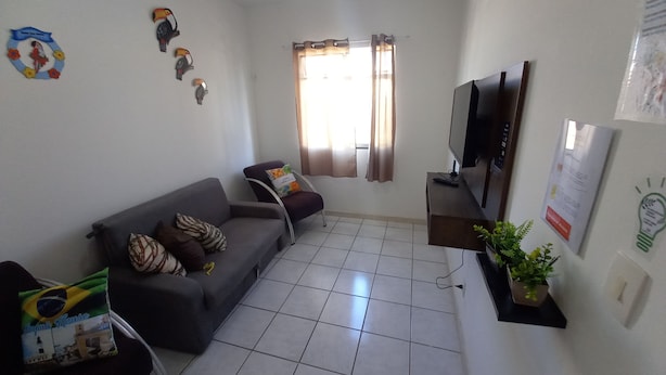 Un saló amb un sofà gris, una televisió, una taula petita i una finestra amb cortines.