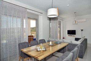 A modern living room with a wooden dining table, grey sofas, and a TV mounted on the wall.