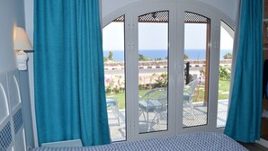 Ein Schlafzimmer mit großem Fenster, das auf einen Garten und das Meer blickt.