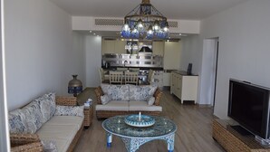 Ein Wohnzimmer mit Sofa, Couchtisch, Fernseher und einer Küche im Hintergrund.