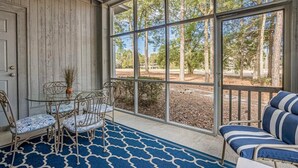 A covered porch with a glass door, a metal table with chairs, and a striped sofa.