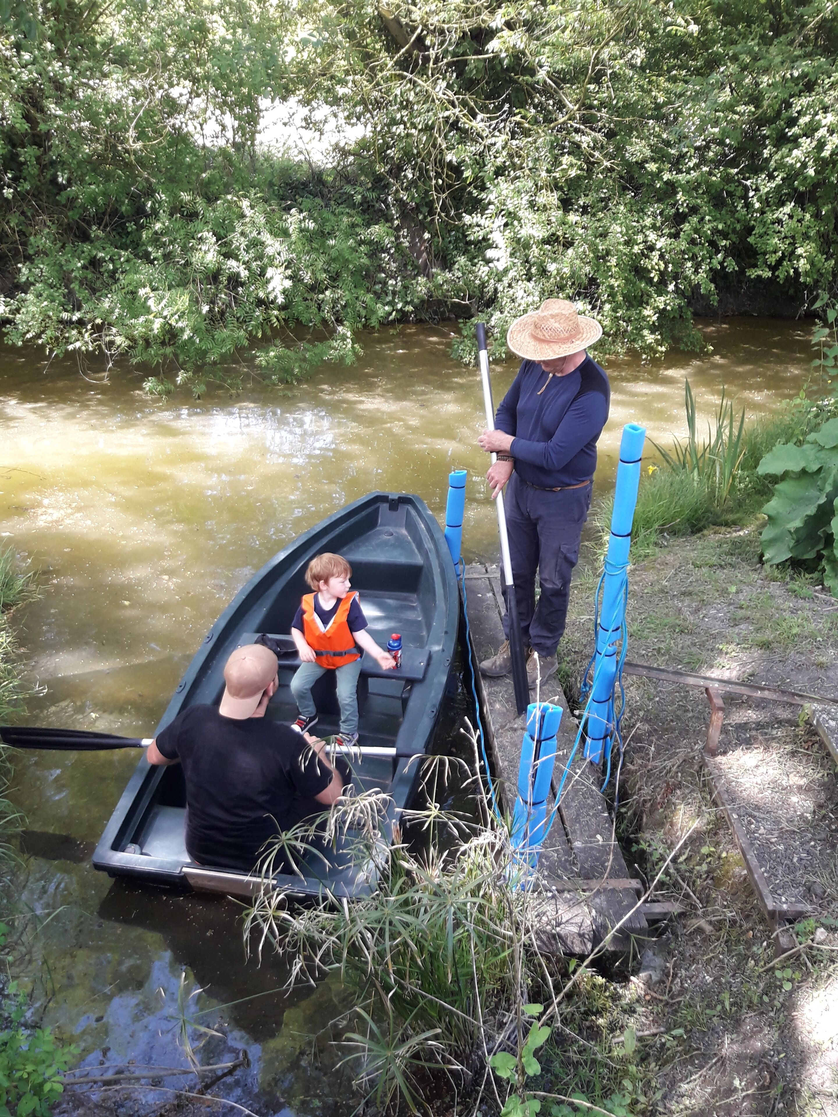 A narrow waterway with a small boat, a person in a straw hat, and another person in a life jacket.