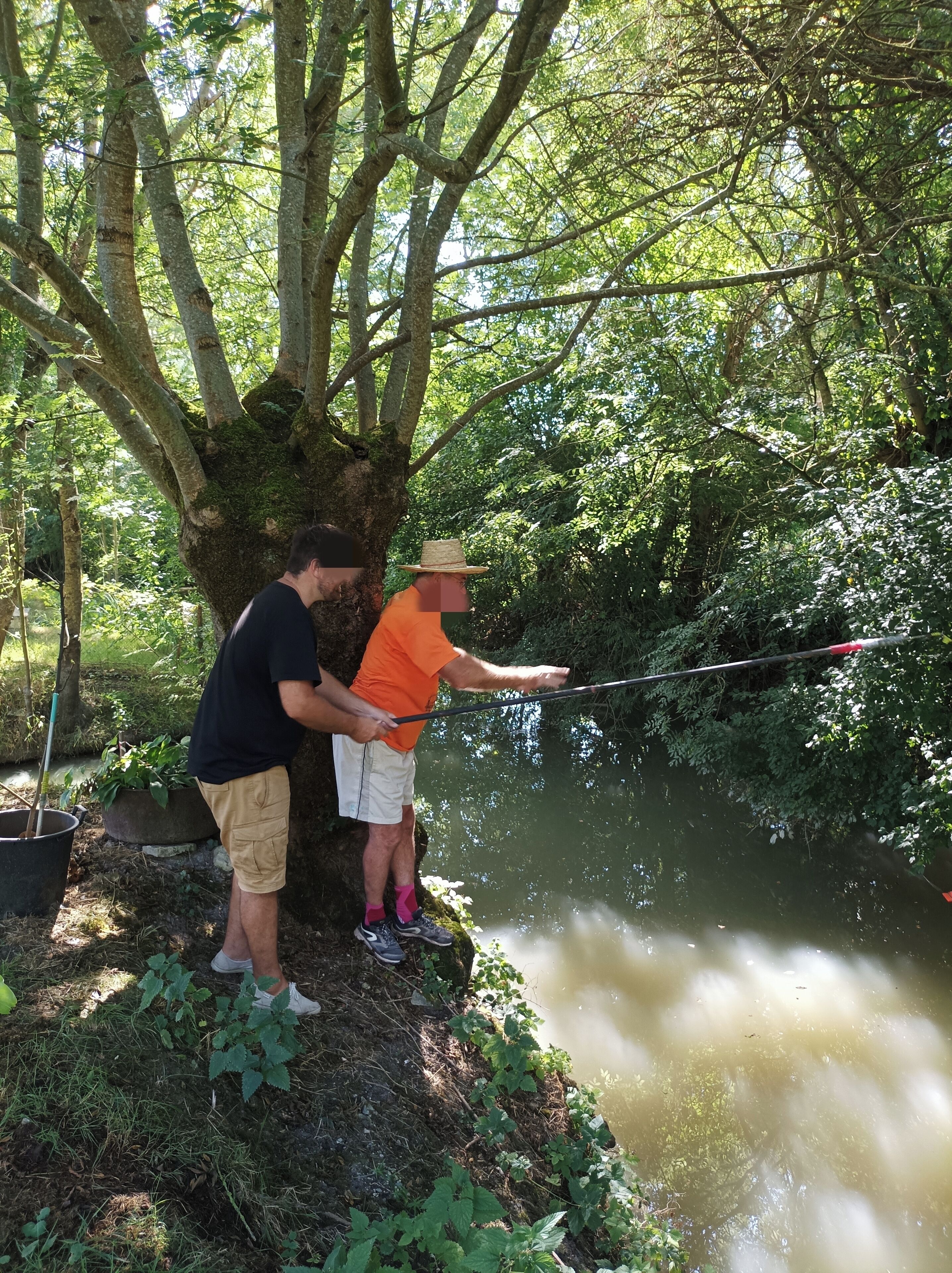 Due persone pescano in un fiume tranquillo, circondato da una fitta vegetazione.