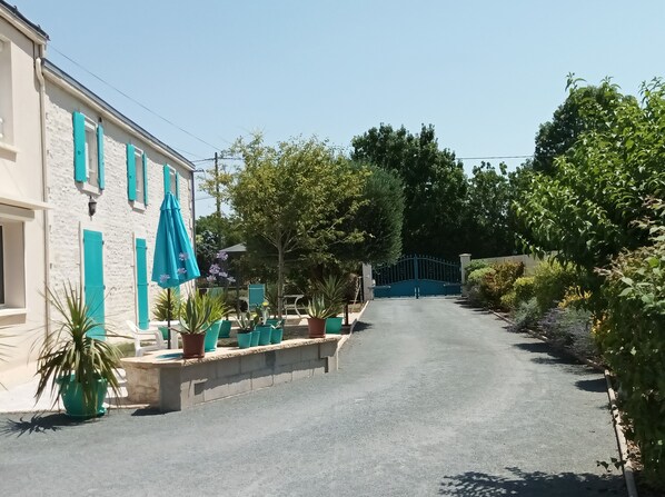 A narrow street with a building on the left, potted plants, and a blue gate at the end.