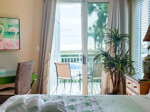 Relax in a tranquil retreat with a large bed, a comfortable chair, and a potted plant, offering a view of the pool and palm trees.