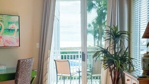 A hotel room with a bed, a chair, a desk, a plant, and a balcony with a view of palm trees. - Oceanfront Villa w/Pool Beach Access Hilton Head (Hilton Head Island)