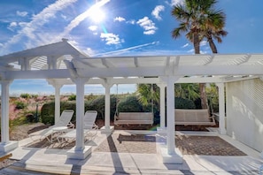 Relax in a serene outdoor space with a pergola, lounge chairs, and a bench, surrounded by lush vegetation and a palm tree.